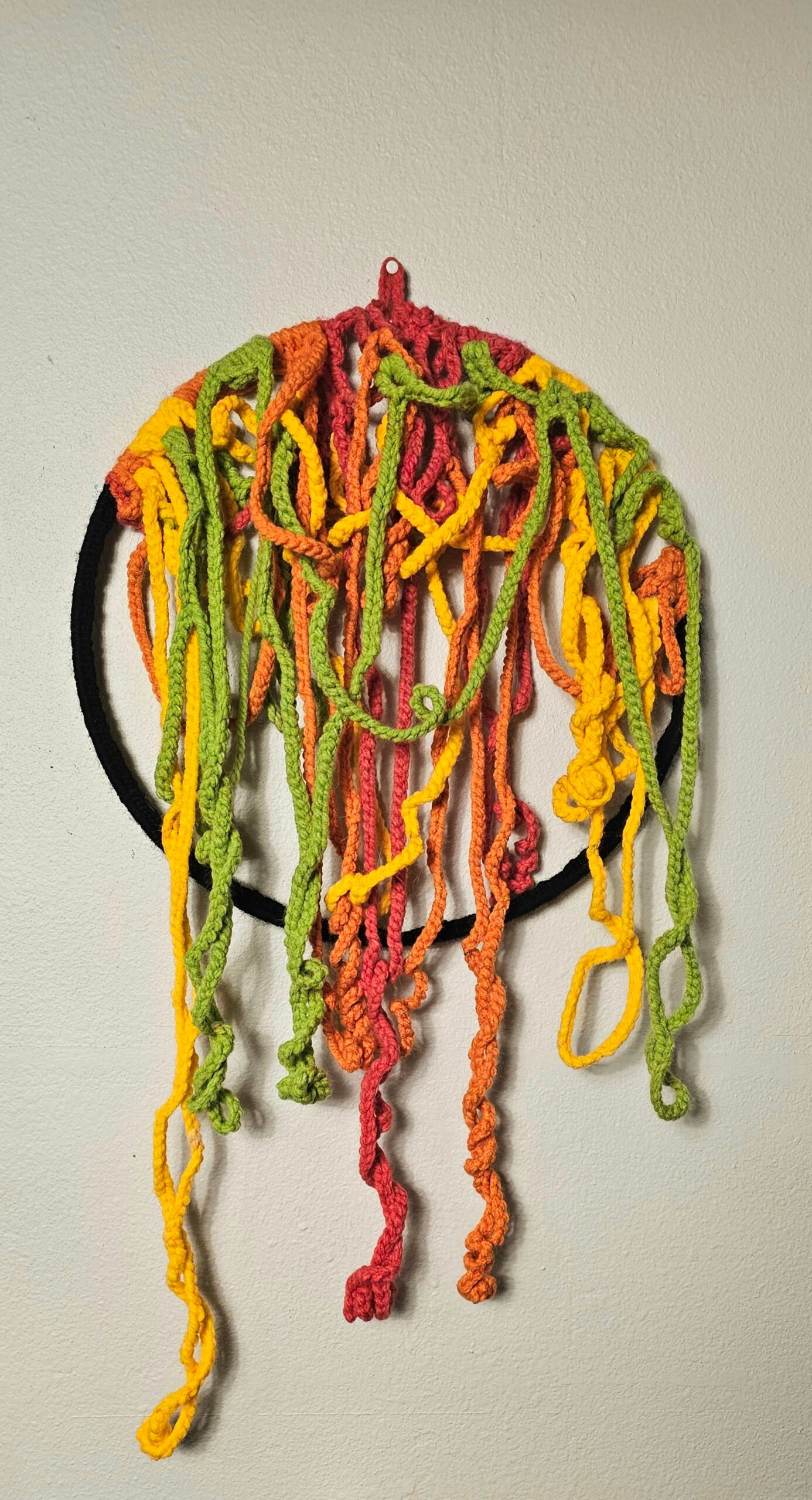 Tangles of red, orange, yellow, and green crocheted cord cascade off of a ring that has been crocheted with black yarn.